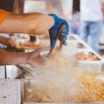 Vendor serving freshly cooked pad Thai noodles at a bustling Bangkok night market with steam rising from hot trays, capturing the vibrant street food scene in Southeast Asia.