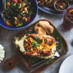 Malaysian and Indonesian street food feast featuring grilled prawns, tropical fruit, vegetables, sambal, and iced drinks served on a communal dining table